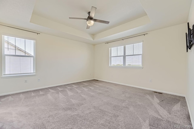 unfurnished room with visible vents, baseboards, a tray ceiling, light carpet, and a ceiling fan