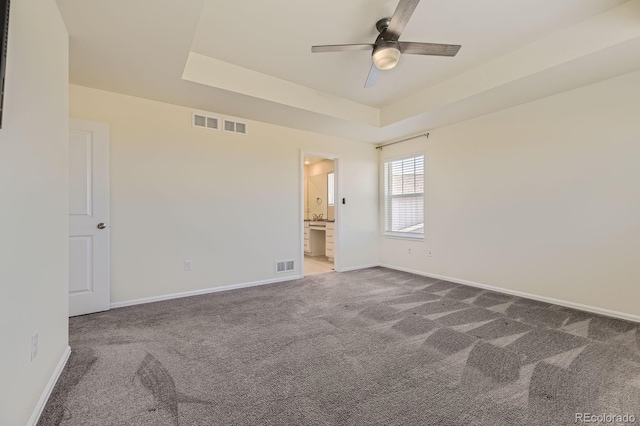 empty room featuring carpet flooring, visible vents, a raised ceiling, and baseboards