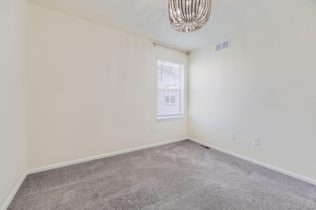 carpeted empty room with visible vents, baseboards, and an inviting chandelier