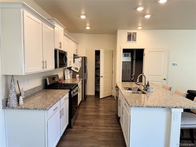 kitchen with a breakfast bar, sink, appliances with stainless steel finishes, a kitchen island with sink, and white cabinets