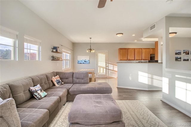 living room featuring ceiling fan with notable chandelier, wood finished floors, visible vents, and baseboards