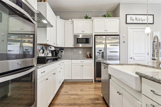 kitchen featuring light hardwood / wood-style flooring, appliances with stainless steel finishes, hanging light fixtures, light stone countertops, and white cabinets