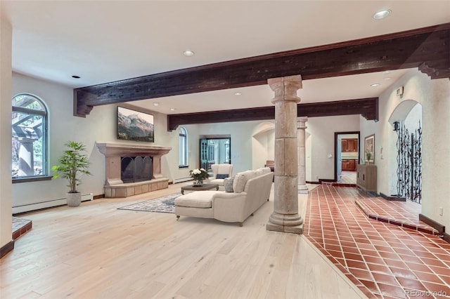 living room with decorative columns, wood finished floors, arched walkways, and a fireplace with raised hearth