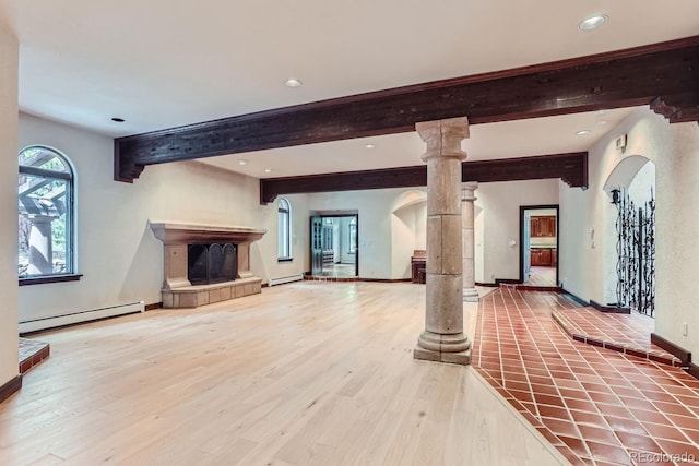 unfurnished living room featuring a fireplace with raised hearth, a baseboard heating unit, decorative columns, wood finished floors, and arched walkways