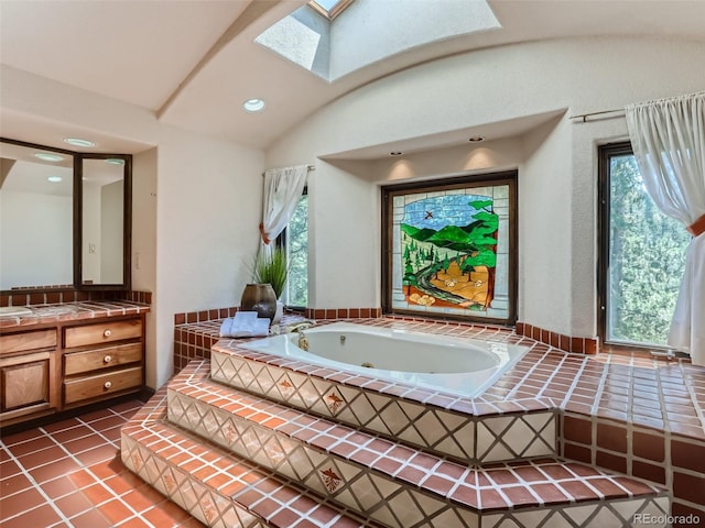 bathroom with tile patterned flooring, vaulted ceiling with skylight, a jetted tub, and vanity