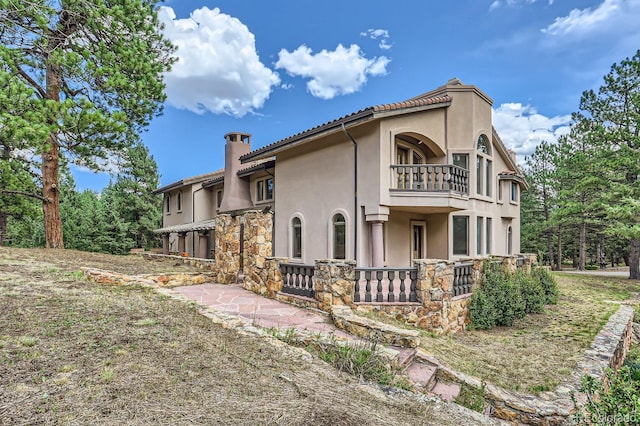 rear view of property with stucco siding, a balcony, and a chimney