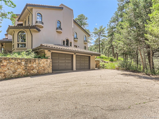 view of side of home featuring a tiled roof, a garage, driveway, and stucco siding