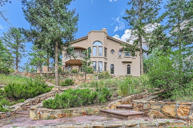 rear view of property featuring a balcony, a chimney, and stucco siding