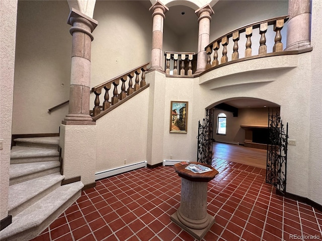 staircase featuring a baseboard heating unit, a high ceiling, baseboards, and arched walkways