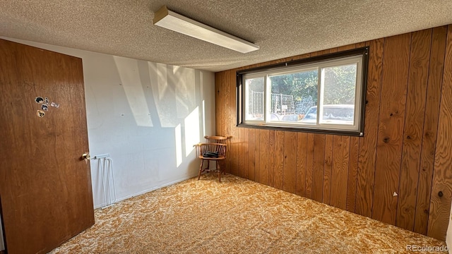 carpeted empty room featuring a textured ceiling and wooden walls