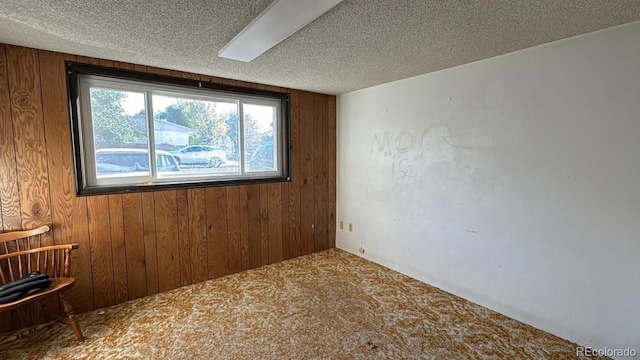 carpeted spare room with a textured ceiling and wood walls