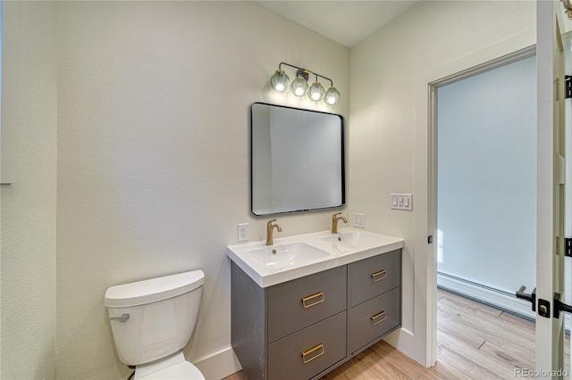 bathroom with wood-type flooring, vanity, a baseboard radiator, and toilet