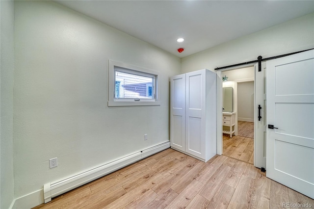 unfurnished bedroom with a barn door, light hardwood / wood-style floors, and a baseboard heating unit