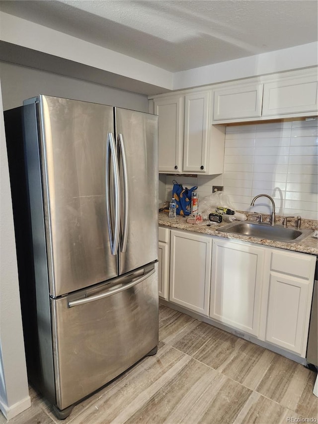 kitchen with tasteful backsplash, white cabinets, freestanding refrigerator, light wood-type flooring, and a sink