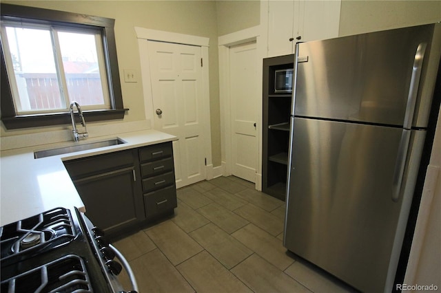 kitchen with stainless steel fridge, range, white cabinetry, and sink