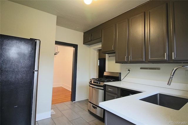 kitchen with light tile patterned flooring, dark brown cabinetry, stainless steel appliances, and sink