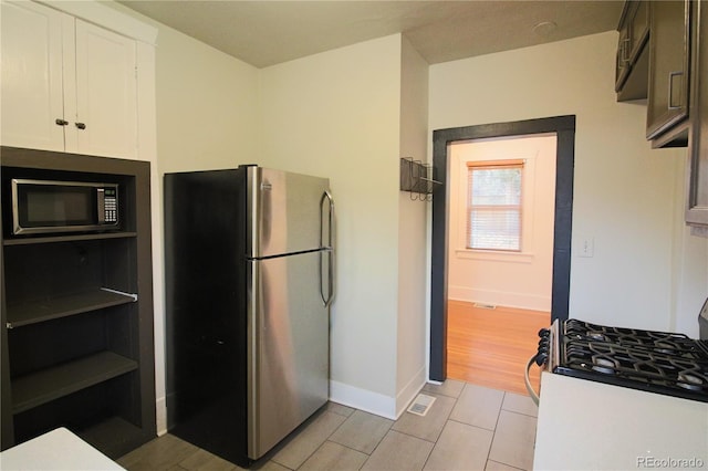 kitchen featuring stainless steel fridge, white gas range, dark brown cabinetry, light tile patterned floors, and white cabinets