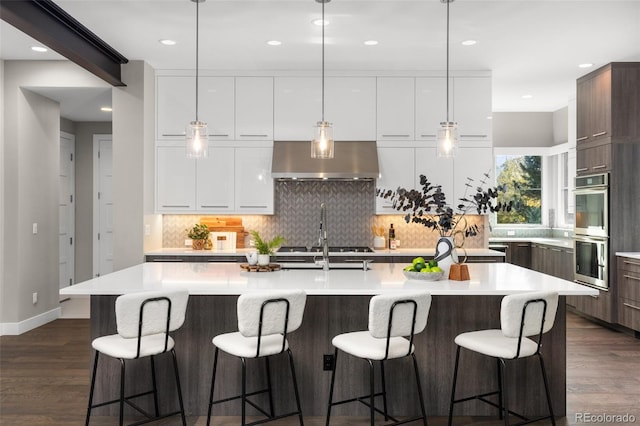 kitchen featuring white cabinetry, appliances with stainless steel finishes, a center island with sink, and wall chimney exhaust hood