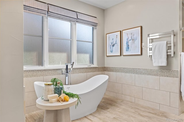 bathroom with tile walls, wood-type flooring, and a bathing tub