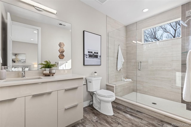 bathroom featuring wood-type flooring, toilet, a shower with door, and vanity