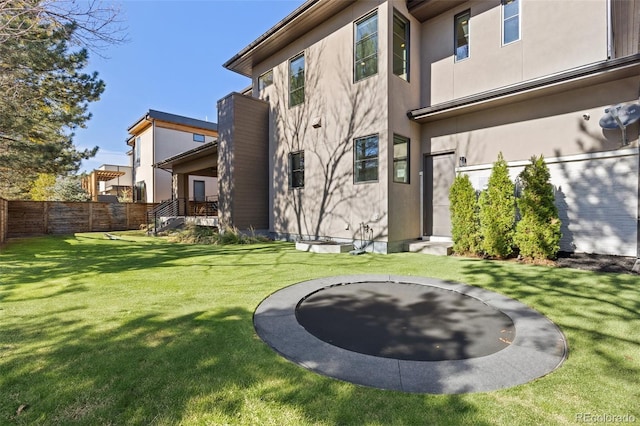 rear view of property featuring a trampoline and a lawn