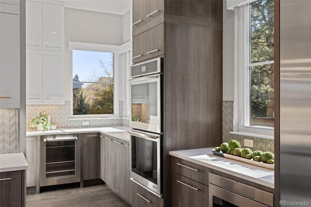 kitchen featuring wine cooler, dark brown cabinetry, stainless steel appliances, and white cabinets