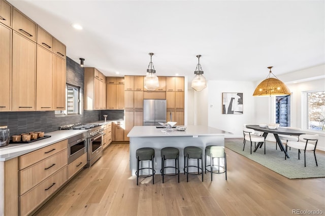 kitchen with a center island, light brown cabinets, backsplash, pendant lighting, and appliances with stainless steel finishes