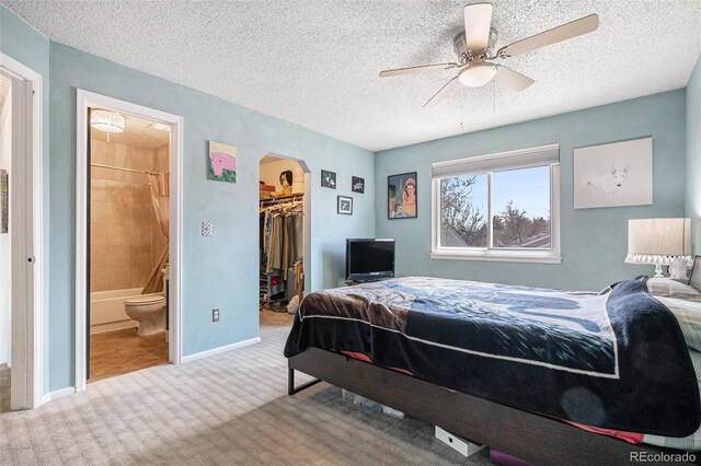 carpeted bedroom featuring arched walkways, a textured ceiling, baseboards, a spacious closet, and a closet