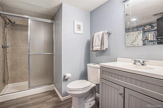 bathroom with a textured ceiling, a textured wall, a shower stall, and wood finished floors