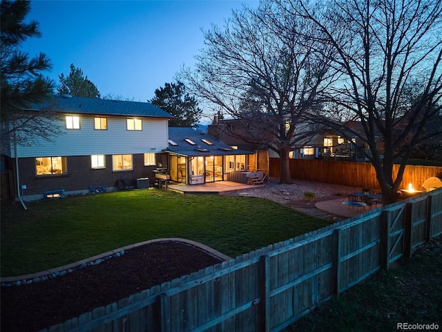 back of house at dusk with brick siding, a fenced backyard, central air condition unit, and a yard