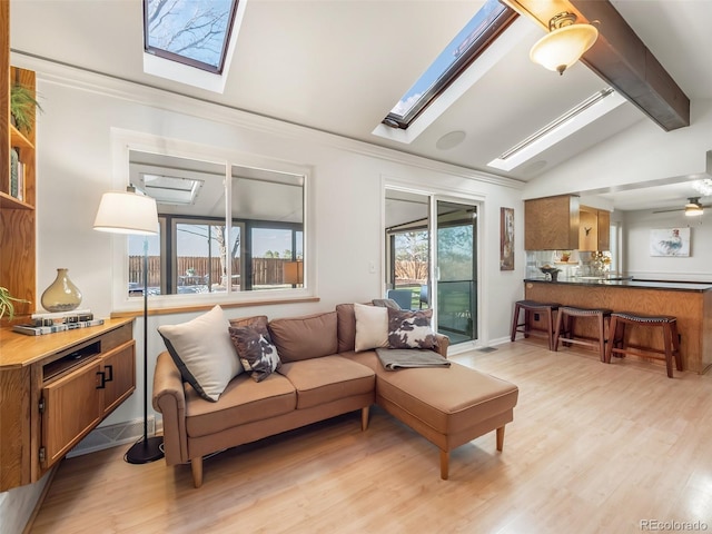 living area featuring vaulted ceiling with skylight, crown molding, and light wood finished floors