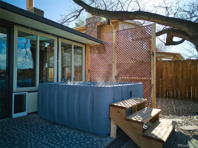 exterior space with a hot tub, fence, and a chimney