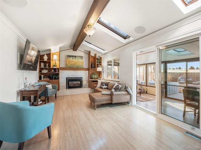 living area featuring crown molding, a premium fireplace, wood finished floors, visible vents, and lofted ceiling with skylight
