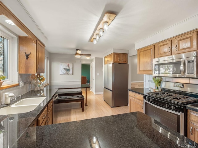 kitchen with brown cabinets, appliances with stainless steel finishes, a sink, light wood-style floors, and decorative backsplash