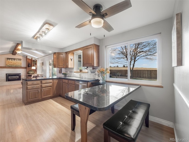 kitchen featuring a peninsula, ceiling fan, brown cabinets, light wood-style flooring, and dishwasher