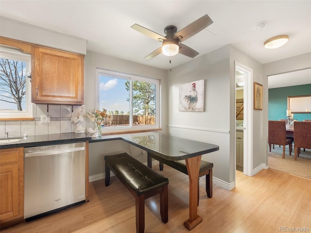 interior space with dark countertops, light wood-style floors, a ceiling fan, baseboards, and stainless steel dishwasher