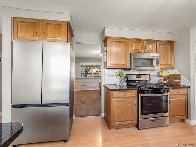 kitchen with dark stone counters, stainless steel appliances, decorative backsplash, and light wood-style floors