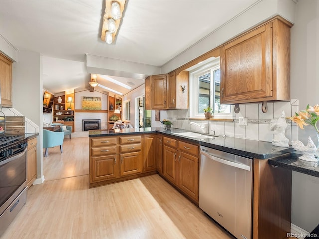 kitchen featuring appliances with stainless steel finishes, a fireplace, a sink, a peninsula, and light wood-style flooring