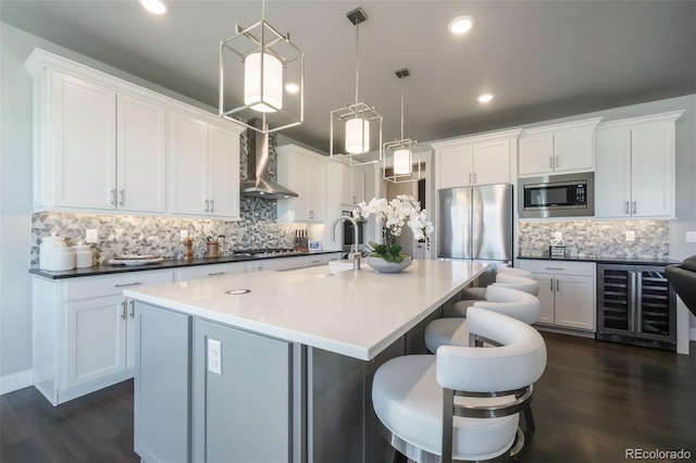 kitchen with beverage cooler, stainless steel appliances, dark wood-type flooring, wall chimney exhaust hood, and a center island with sink