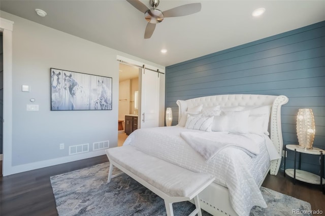 bedroom with visible vents, a barn door, wooden walls, wood finished floors, and baseboards