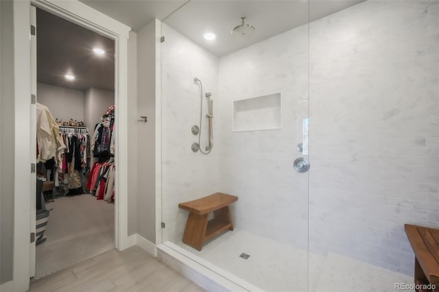 bathroom with a spacious closet, tiled shower, and wood finished floors