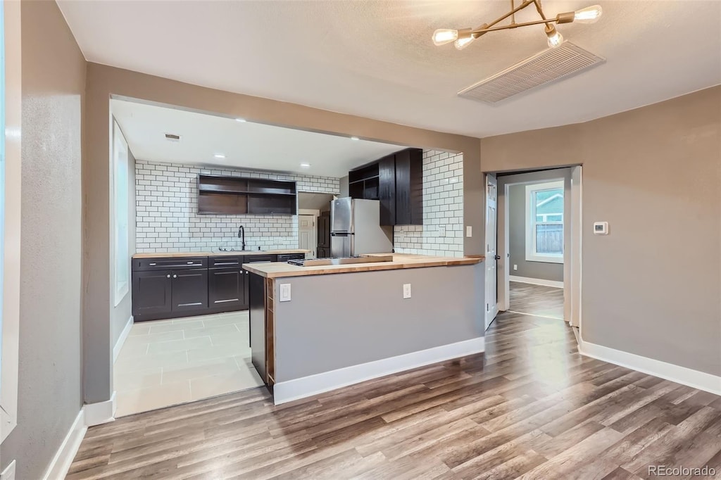 kitchen with wooden counters, sink, light wood-type flooring, tasteful backsplash, and stainless steel refrigerator