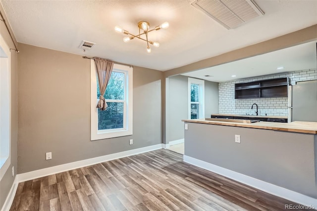 kitchen with an inviting chandelier, sink, hardwood / wood-style flooring, stainless steel fridge, and tasteful backsplash