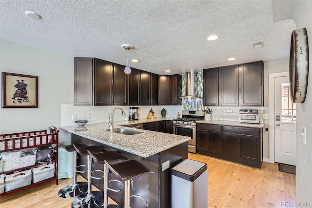 2901 N Glencoe St, Denver, CO 80207 - kitchen featuring gas stove, a sink, wall chimney exhaust hood, a peninsula, and dark brown cabinetry