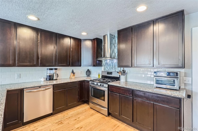 2901 N Glencoe St, Denver, CO 80207 - kitchen featuring appliances with stainless steel finishes, wall chimney exhaust hood, a textured ceiling, dark brown cabinetry, and light wood-type flooring