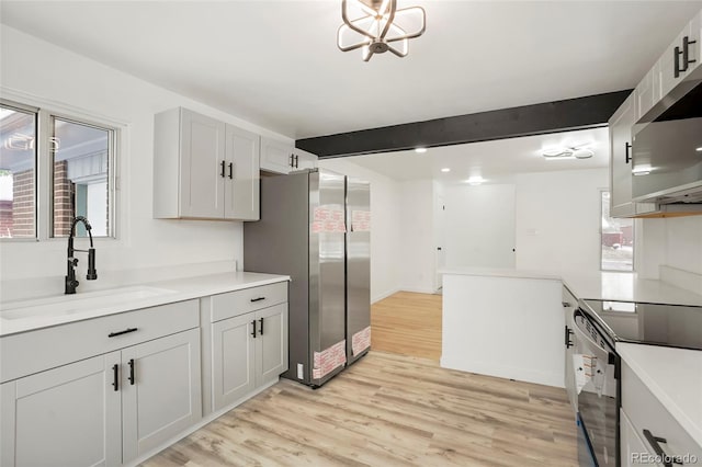 kitchen featuring sink, light wood-type flooring, appliances with stainless steel finishes, a notable chandelier, and beam ceiling