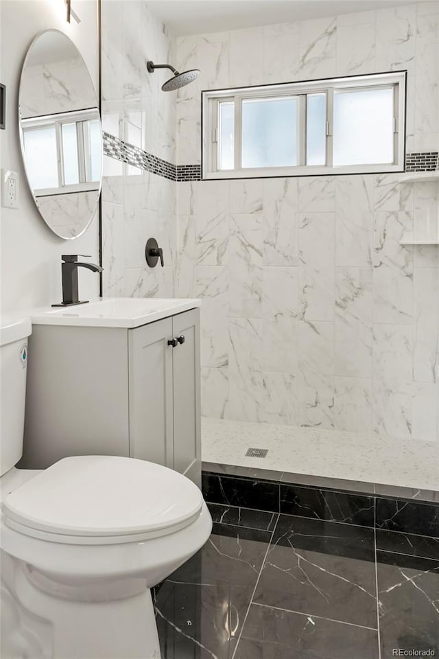 bathroom featuring a tile shower, vanity, and toilet