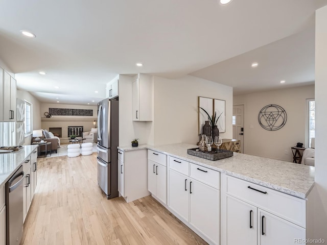 kitchen with stainless steel appliances, light stone counters, light hardwood / wood-style floors, white cabinets, and kitchen peninsula