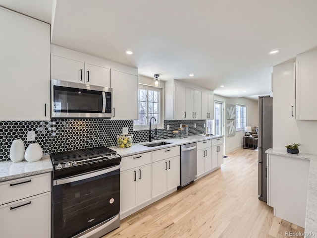 kitchen with sink, appliances with stainless steel finishes, light stone countertops, light hardwood / wood-style floors, and white cabinets