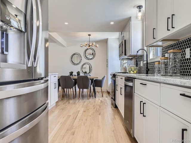 kitchen with white cabinetry, appliances with stainless steel finishes, backsplash, and light wood-type flooring